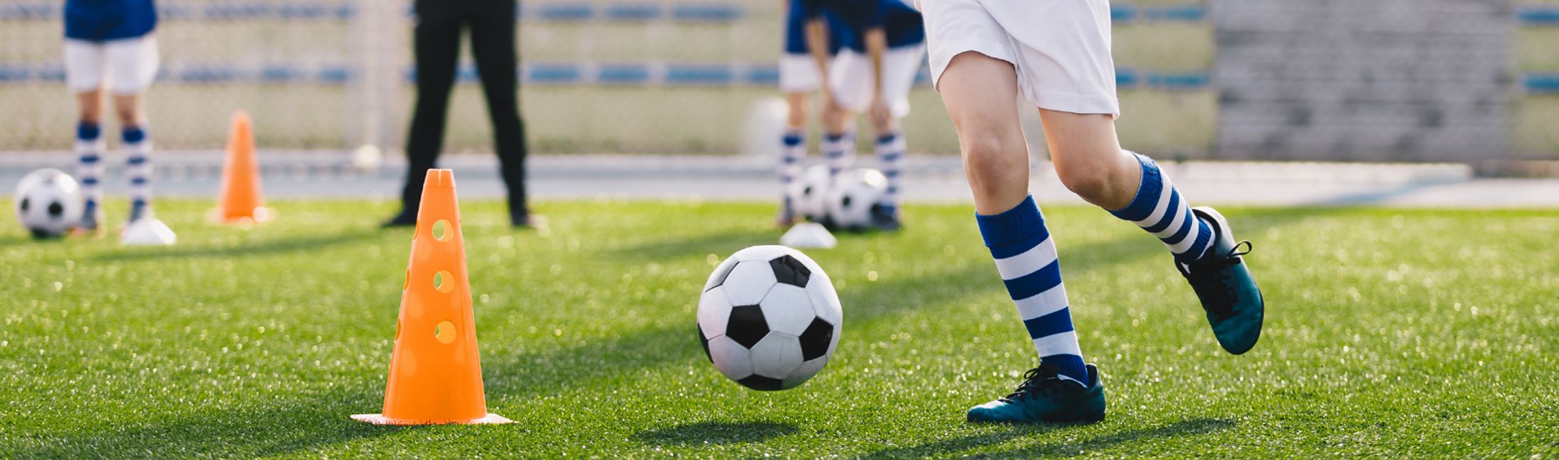 A soccer player kicking a soccer ball with 3 other players and a coach in the background