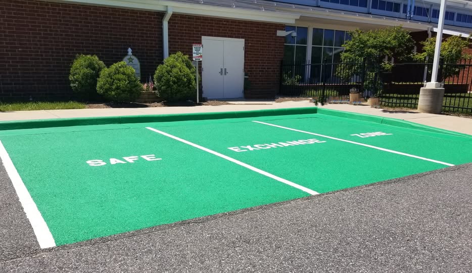 Three parking spaces painted green and designated as the \"Safe Exchange Zone\".